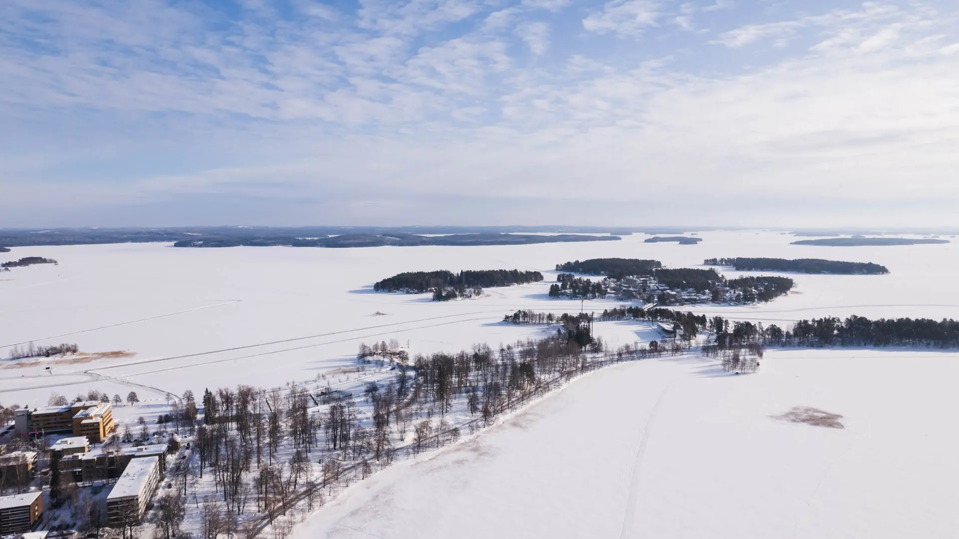 Ilmakuva talvisesta Väinölänniemestä Kuopiossa, lumisten jään ja saarien ympäröimänä.