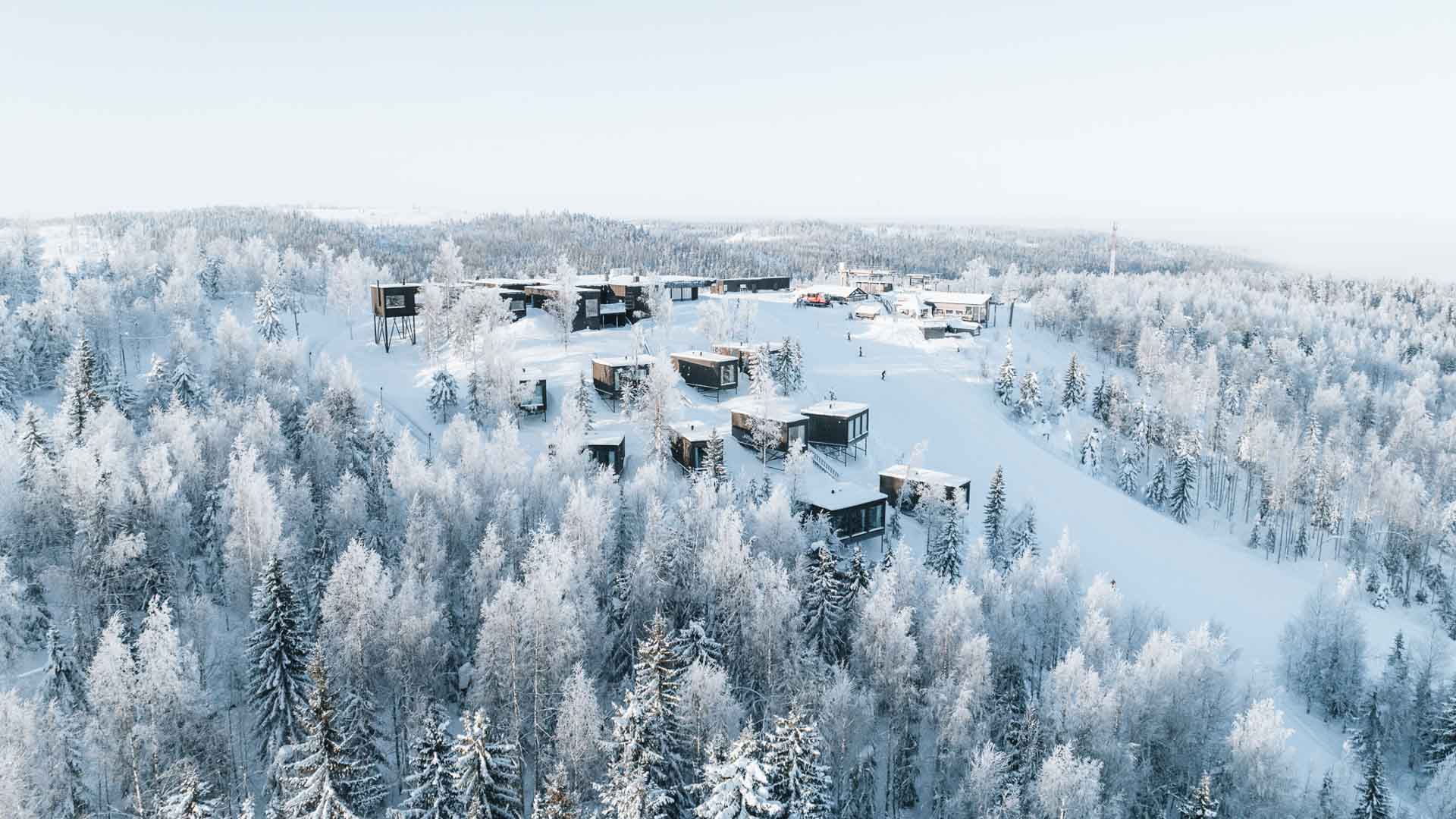 Talvinen ilmakuva Panorama Landscape Hotelista lumisten puiden keskellä rinteessä, taustalla metsäinen maisema.